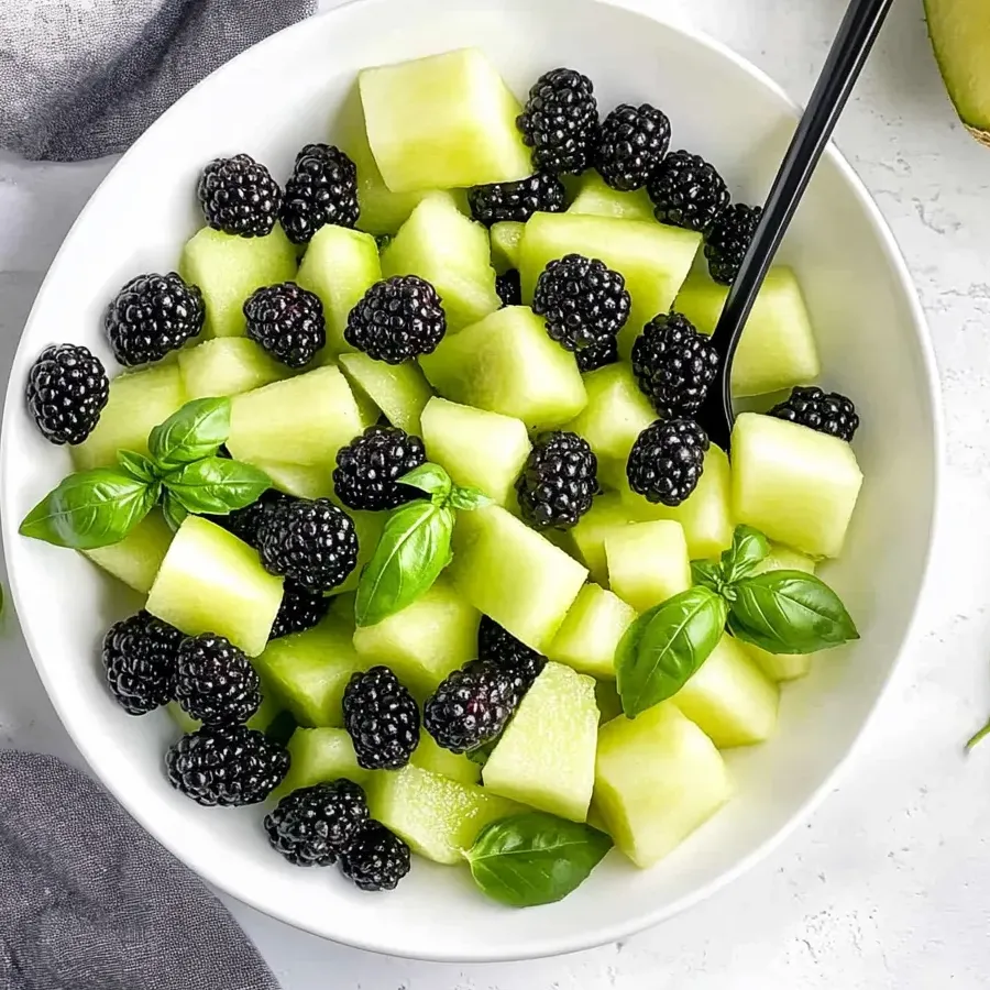 Un bol de salade de fruits avec mûres, melon et basilic.