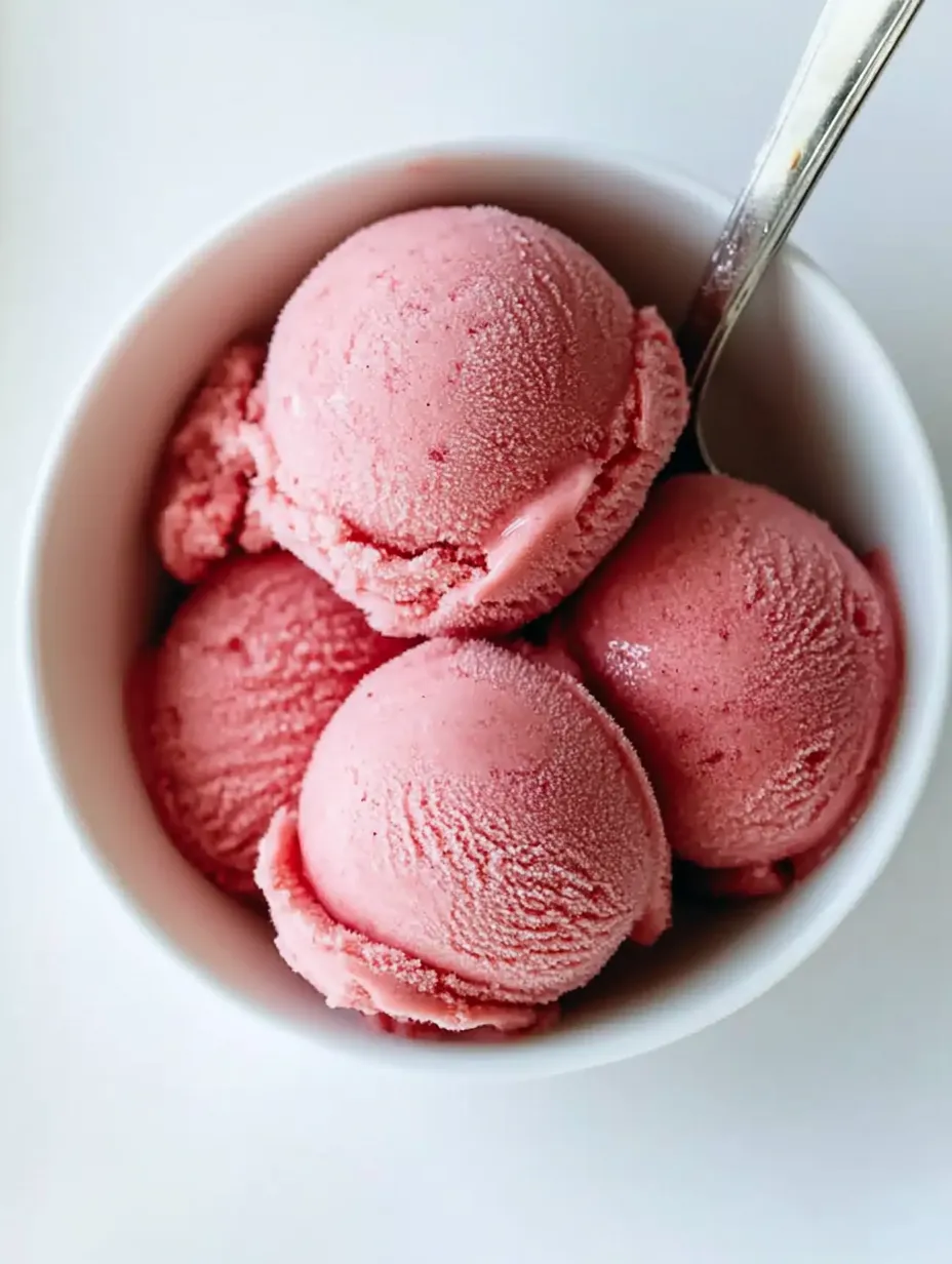 Un bol de yaourt glacé rose avec une cuillère dedans.