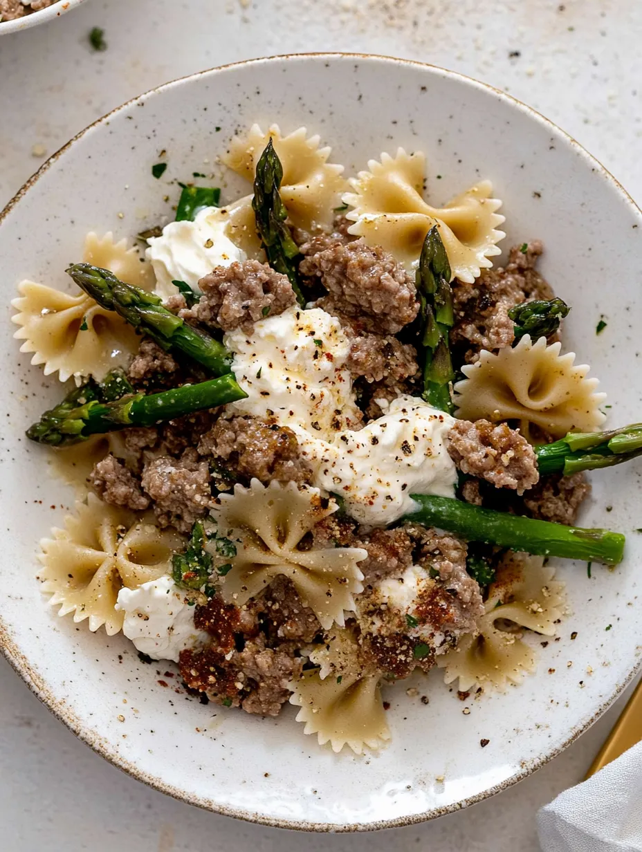 Un bol de pâtes avec saucisse et asperges.