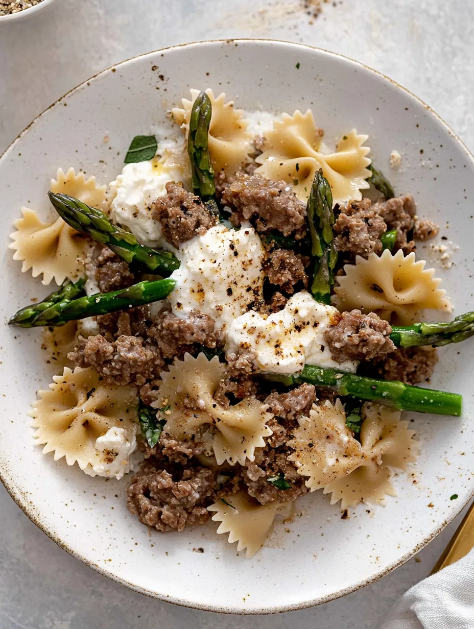 Une assiette de pâtes avec saucisse et asperges.