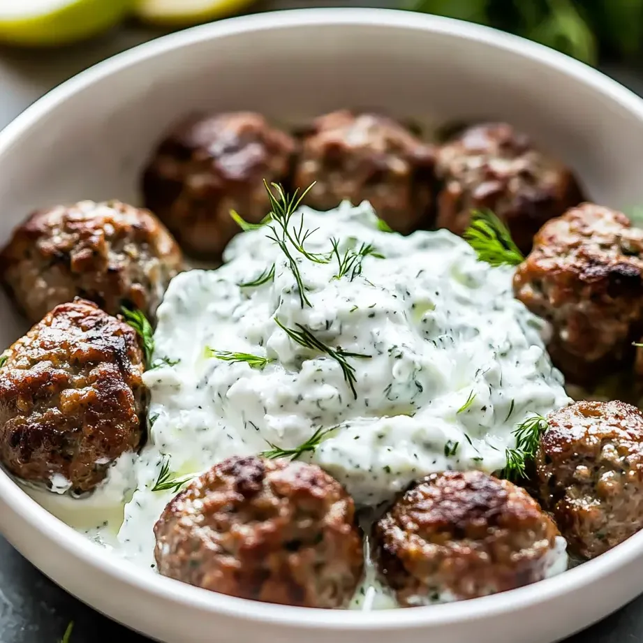 Un bol de boulettes avec une sauce blanche par-dessus.