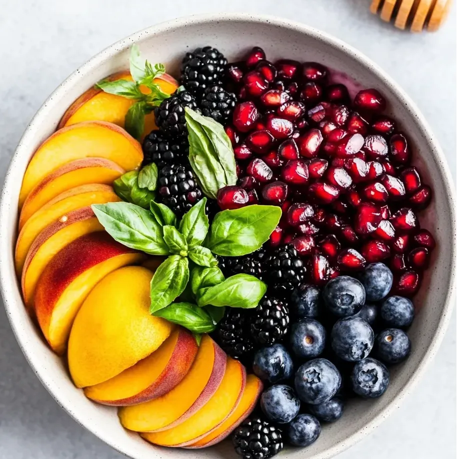 Un bol de fruits avec myrtilles, mûres, pêches et un filet de miel.