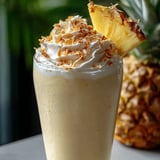 Un verre rempli d’un milkshake à l’ananas, décoré d’une tranche d’ananas sur le dessus.