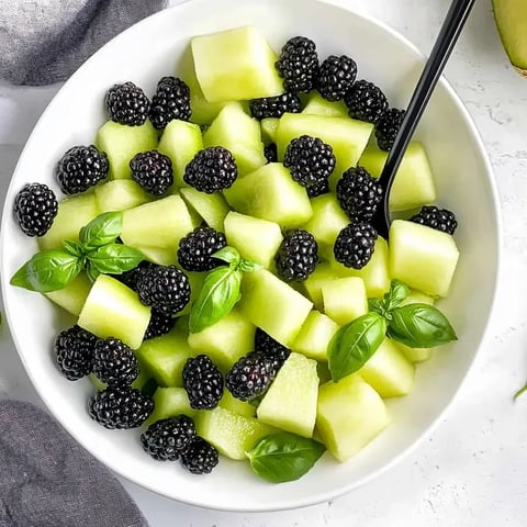 Un bol de salade de fruits avec mûres, melon et basilic.