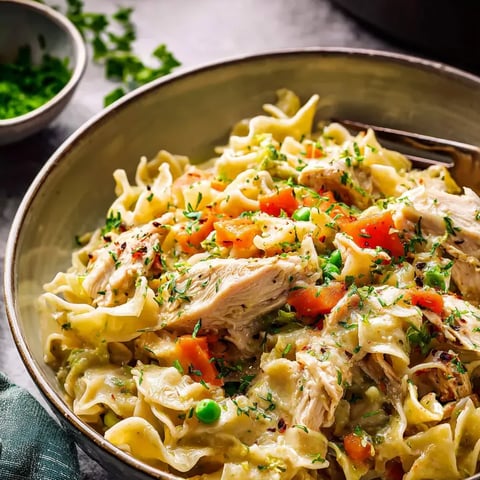 Un bol de pâtes avec du poulet et des légumes.